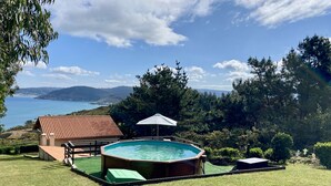 A backyard with a swimming pool, a small house, and a view of the ocean.