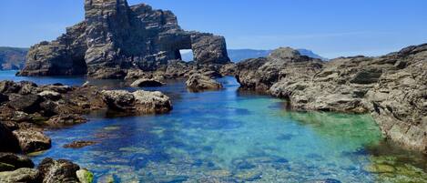 A rocky coastal landscape with clear water and a prominent rock formation.