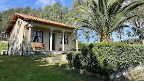 A house with a tiled roof, a front porch with a bench, and a well-maintained garden with a palm tree.