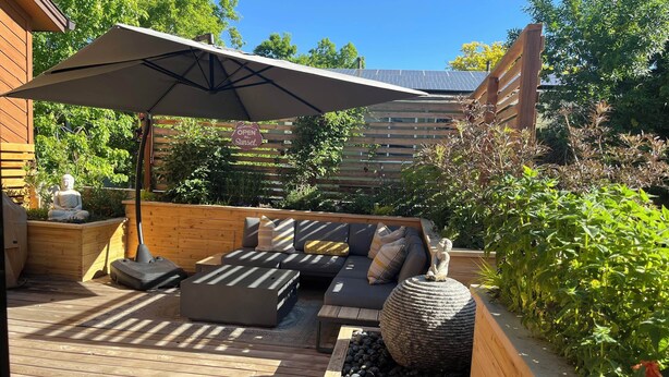 A wooden deck with a sofa and cushions, a large umbrella, and a Buddha statue. - The Buddha House - Luxurious North Boulder Retreat (Boulder)