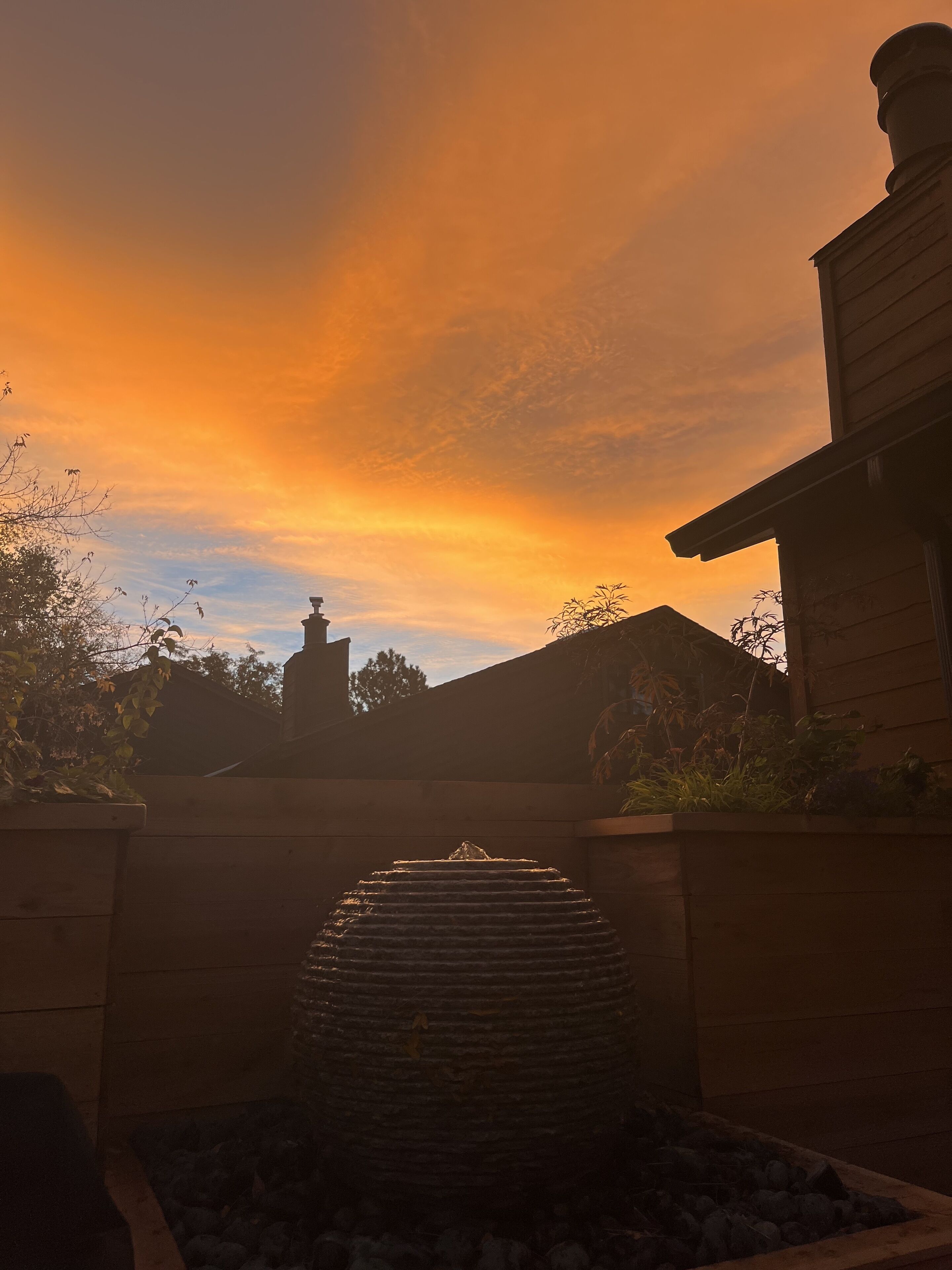 Een fontein van steen in een tuin, met een zonsondergang op de achtergrond.