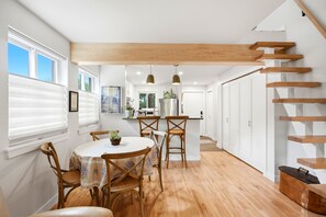 A modern kitchen with wooden beams, a dining area with a round table and chairs, and a staircase with wooden steps.