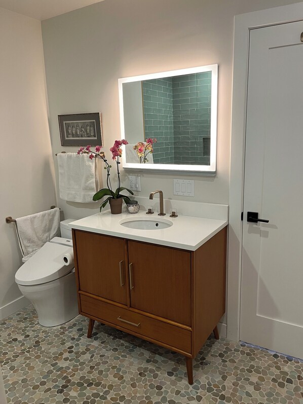 A bathroom with a white toilet, a wooden vanity with a sink, a mirror, and a potted orchid plant.