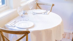 A round dining table set with white tablecloth, plates, cutlery, and glasses, with a wooden chair in the foreground. - The Buddha House - Luxurious North Boulder Retreat (Boulder)