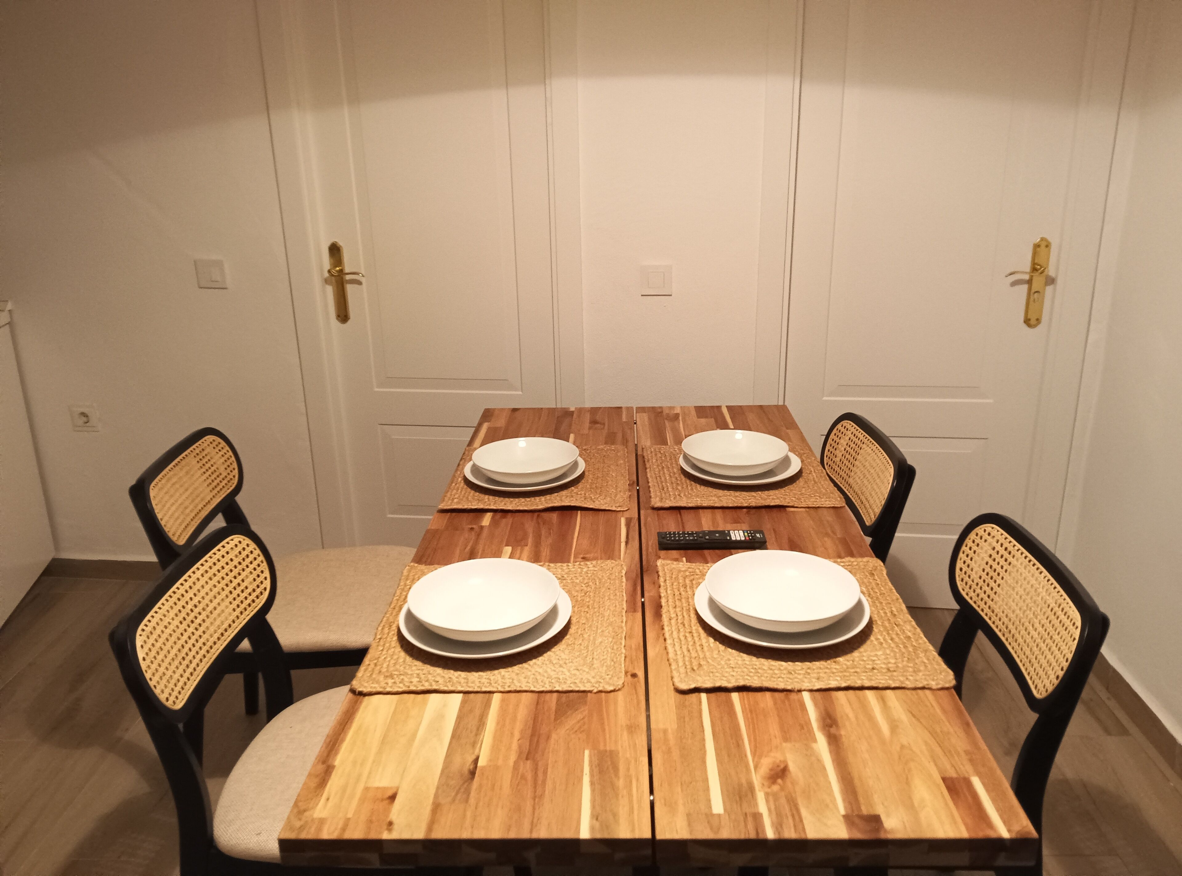 A dining table with four chairs, a remote control, and placemats.
