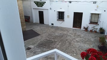 A courtyard with a white building, a sign, potted plants, and a red flower in the foreground.