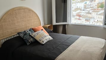 A bed with a curved headboard, a window with a view of buildings, and a bedside table with a lamp.