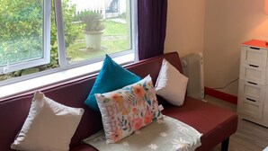A room with a red sofa, a window with curtains, a radiator, and a white cabinet. - Cozy Coastal Apartment in Kilgetty With Views (Kilgetty)
