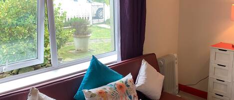 A room with a red sofa, a window with curtains, a radiator, and a white cabinet.
