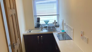 A small kitchen with a window, a sink, cabinets, and a countertop. - Cozy Coastal Apartment in Kilgetty With Views (Kilgetty)