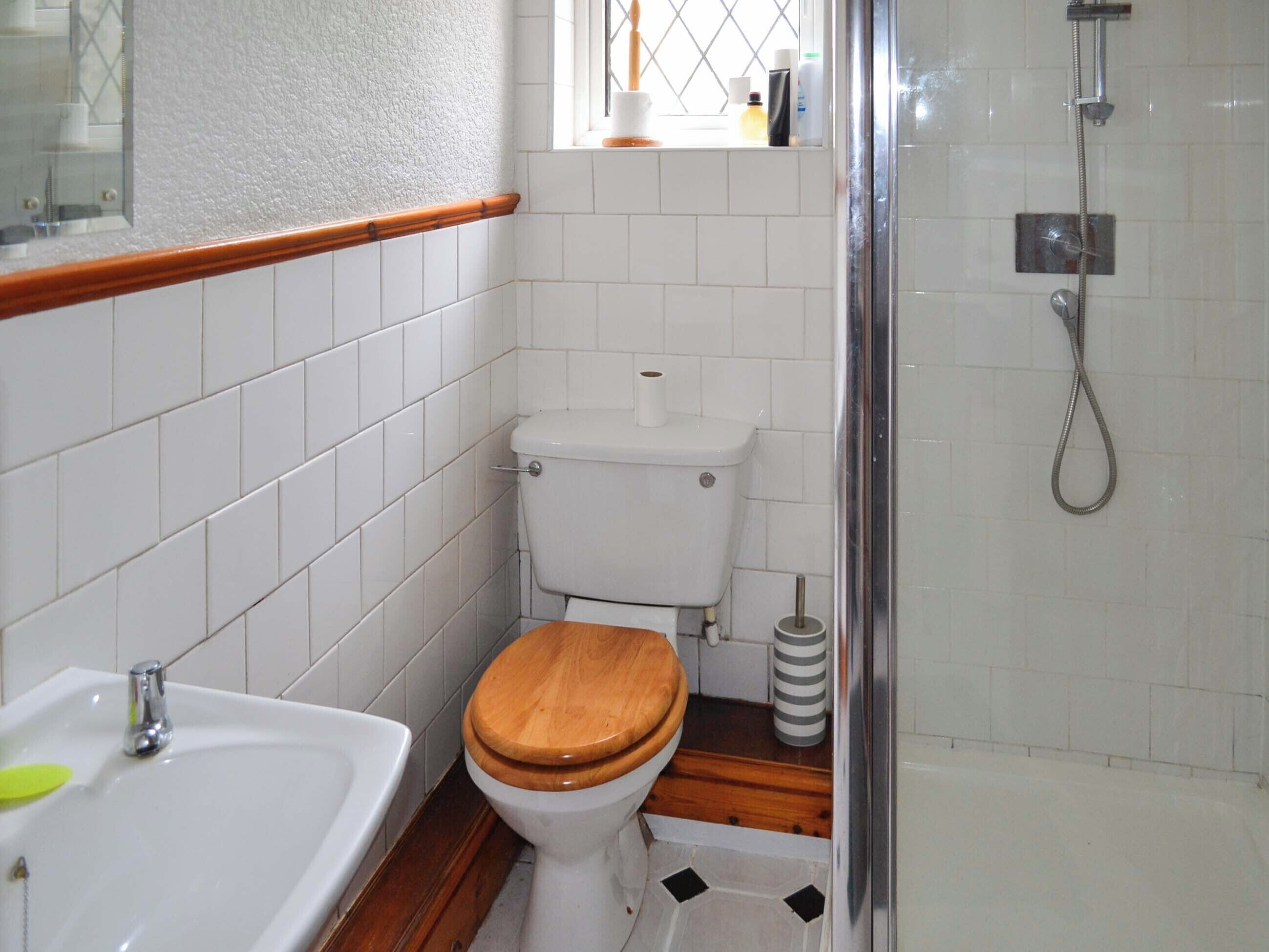 Een kleine badkamer met een wit toilet, een houten wastafel en een douche.