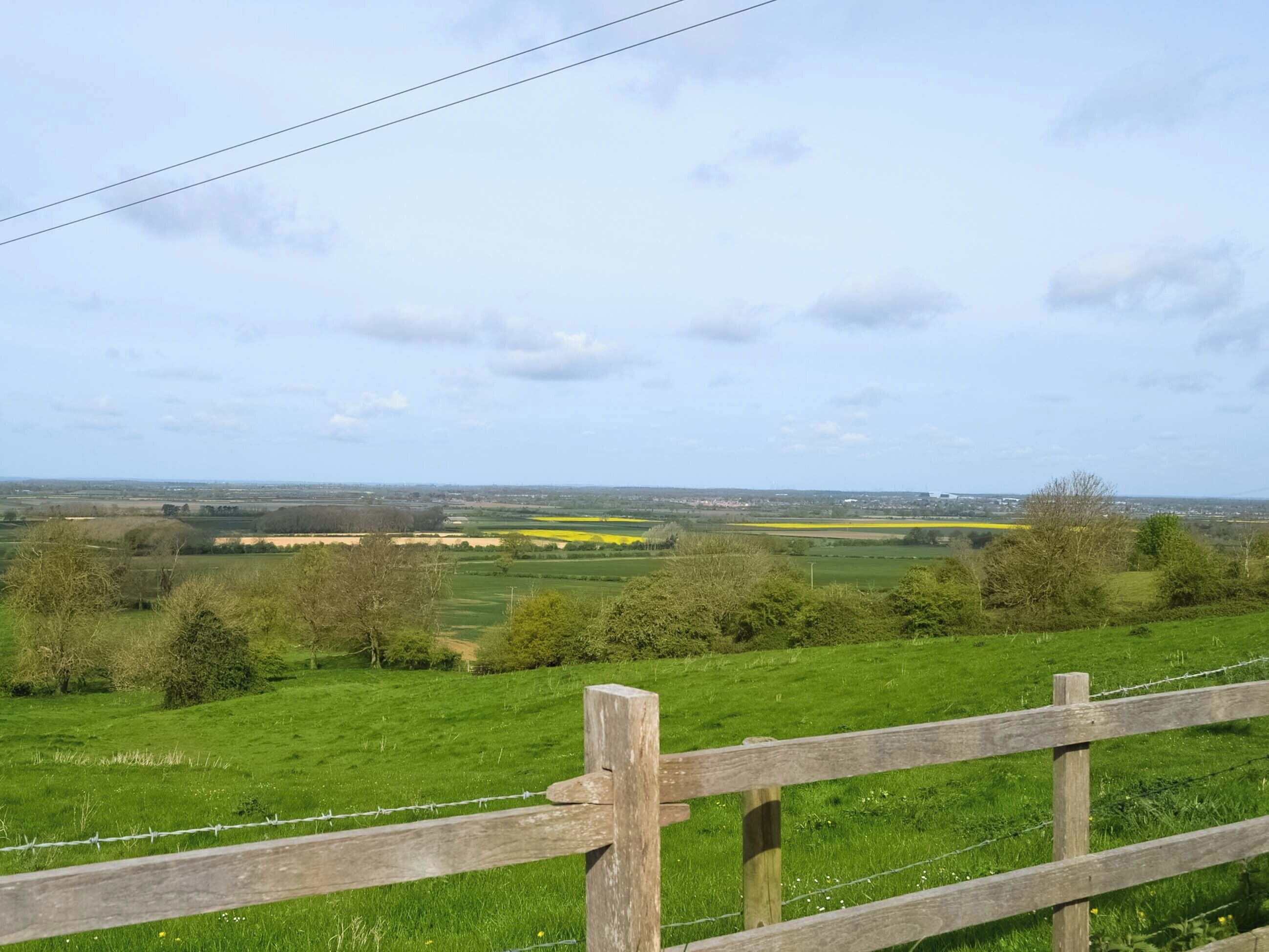 A rural landscape with a wooden fence and barbed wire, fields, and a distant view of a town.