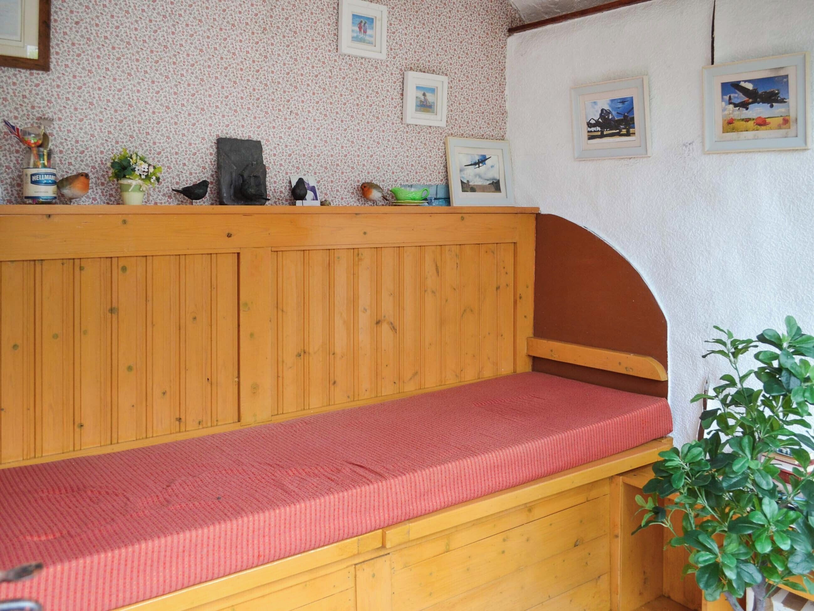 Eine hölzerne Bank mit rotem Kissen in einem Raum mit floralem Wandpapier und gerahmten Bildern an der Wand.