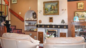 Een gezellige woonkamer met twee witte leren fauteuils, een open haard met decoratieve objecten, en verschillende ingelijste foto's aan de wanden.