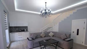 A modern living room with a sectional sofa, a glass coffee table, and a staircase leading to a second floor. - Oscar Hotel (Samarkand)