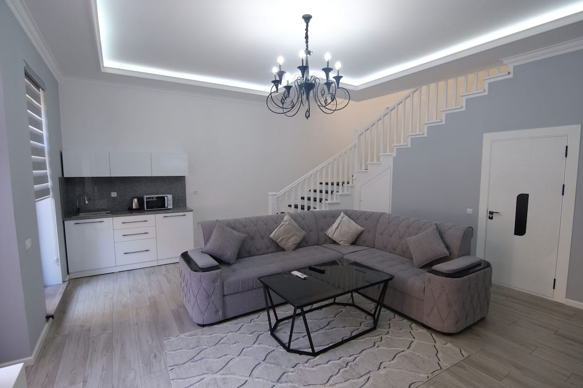 A modern living room with a sectional sofa, a glass coffee table, and a staircase leading to a second floor.