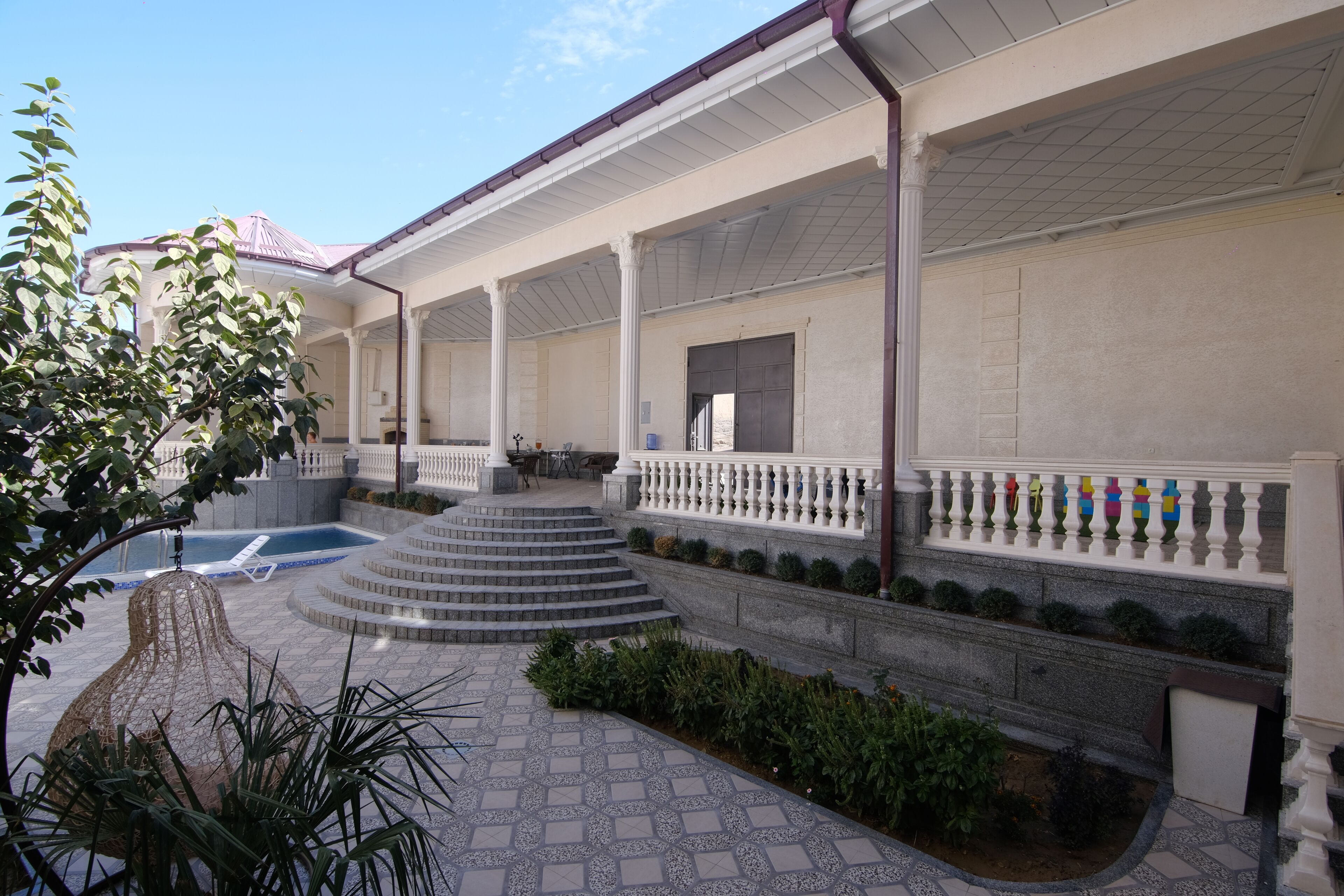 A covered outdoor area with a pool, steps leading to a covered seating area, and a garden with plants and a decorative tree.
