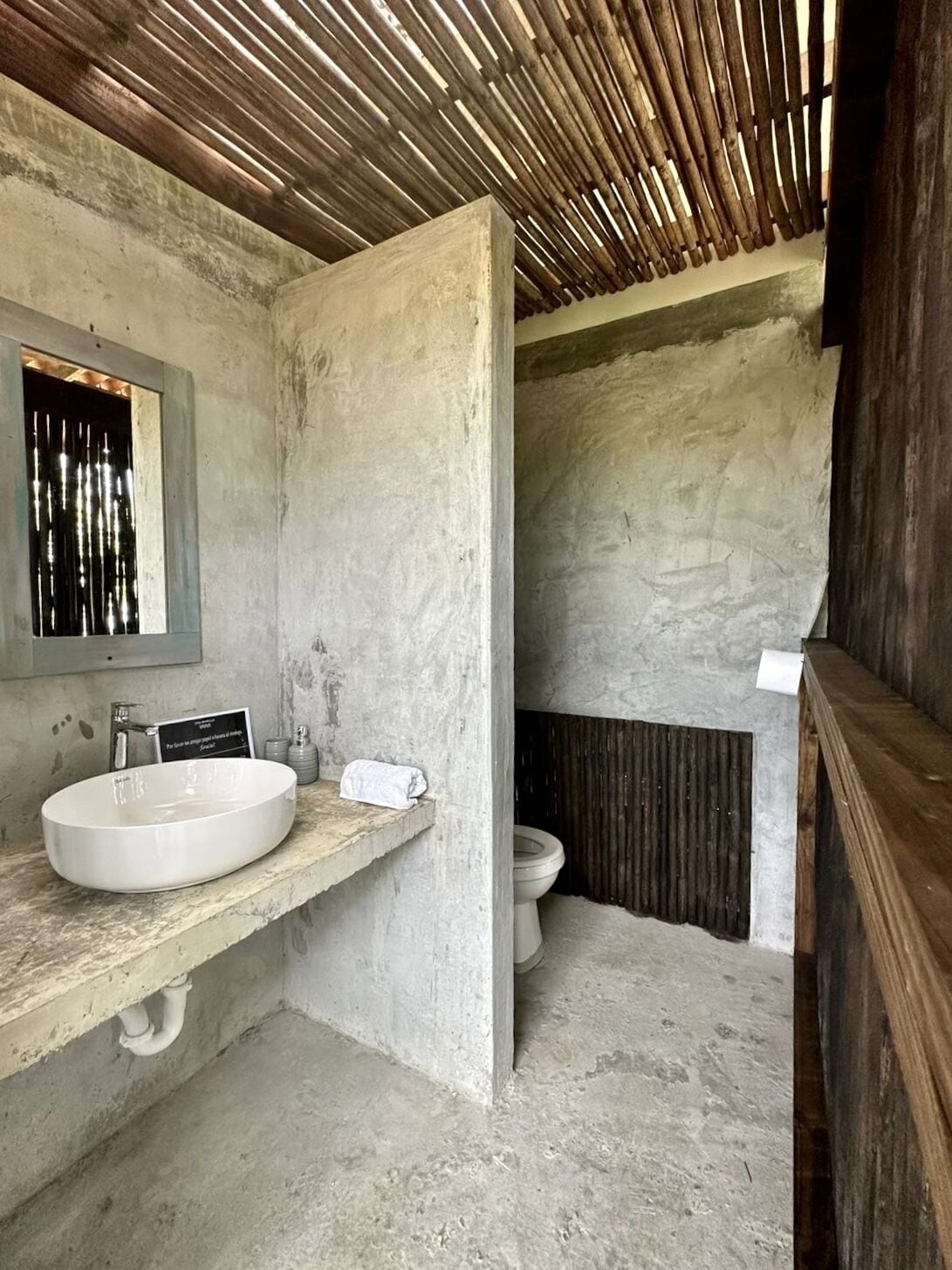 A bathroom with a concrete sink, a toilet, and a wooden ceiling.