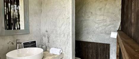 A bathroom with a concrete sink, a toilet, and a wooden ceiling.