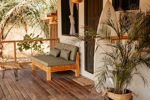 Una terraza de madera con un banco acolchado verde, una planta en maceta y una mesa de madera.