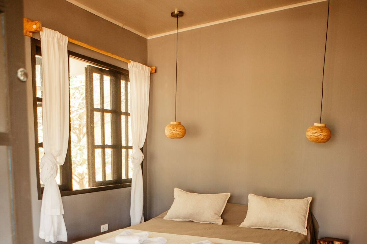 A bedroom with a bed, curtains, a window, and a woven rug.