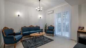 Een woonkamer met een blauwe zithoek, een salontafel en een kroonluchter.