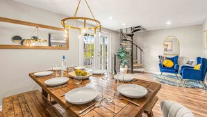 Un espace repas avec une table en bois dressée pour six personnes, un lustre et un escalier menant à un niveau supérieur.