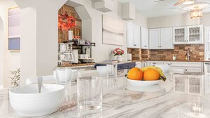 Une cuisine moderne avec des meubles blancs, un plan de travail en marbre et un panier de fruits contenant des oranges et des bananes.