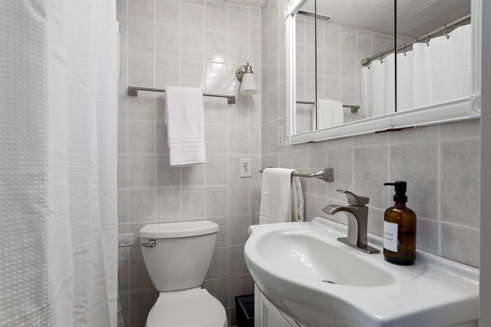 A bathroom with a toilet, a sink, a mirror, and a shower curtain.