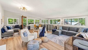 Un salon spacieux avec un grand canapé d’angle, un fauteuil blanc et un coin repas comprenant une table et des chaises.
