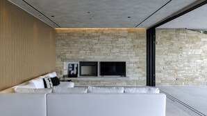 Een moderne woonkamer met een stenen muur, een witte bank en twee flatscreen televisies die aan de muur zijn bevestigd.