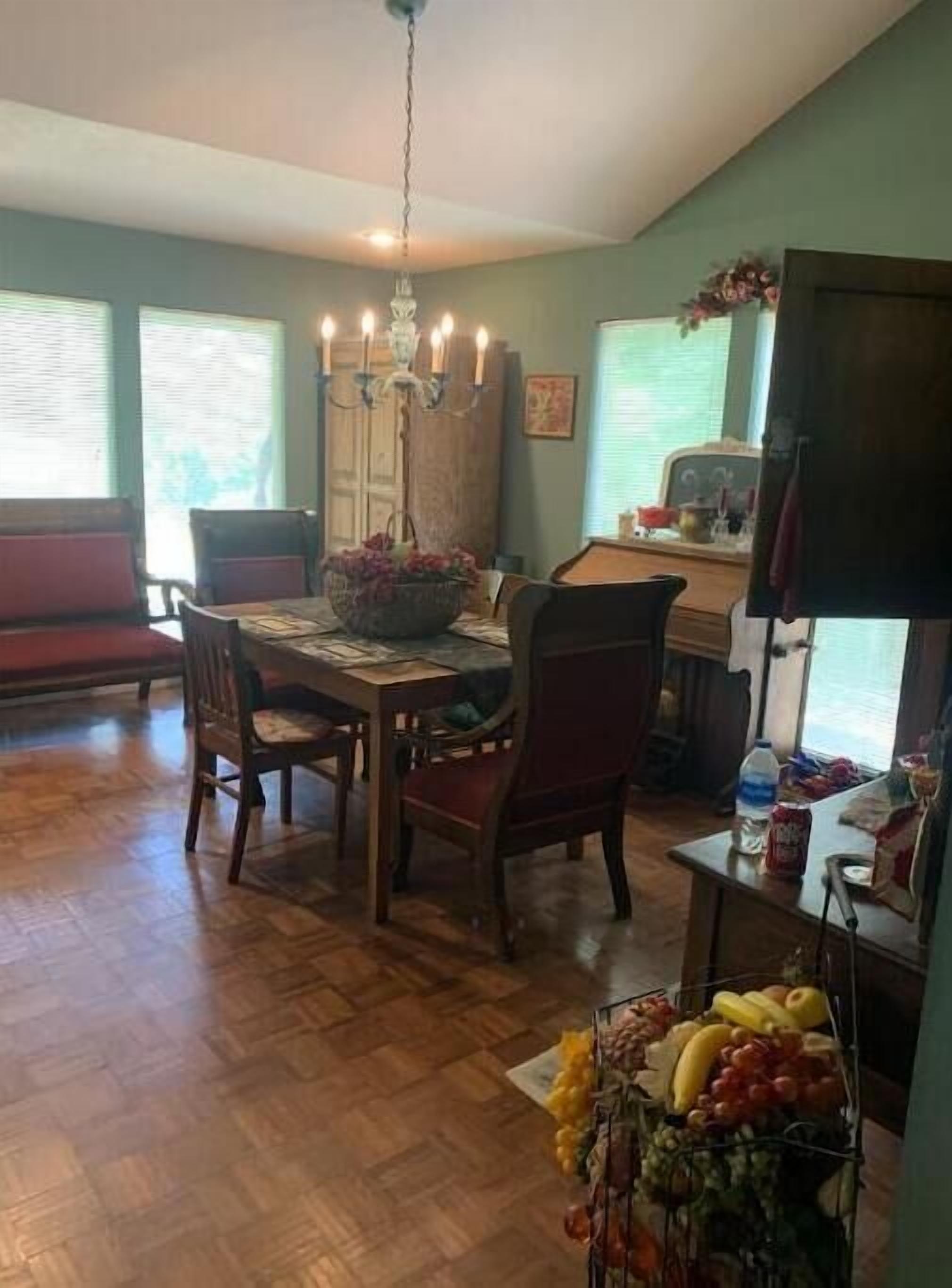 A dining area with a wooden table, chairs, a chandelier, and a fruit basket.