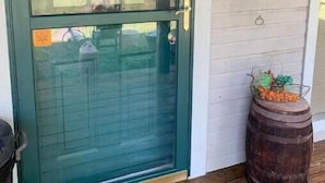 A green door with a glass panel, a metal lantern, and a barrel with vegetables on the porch.