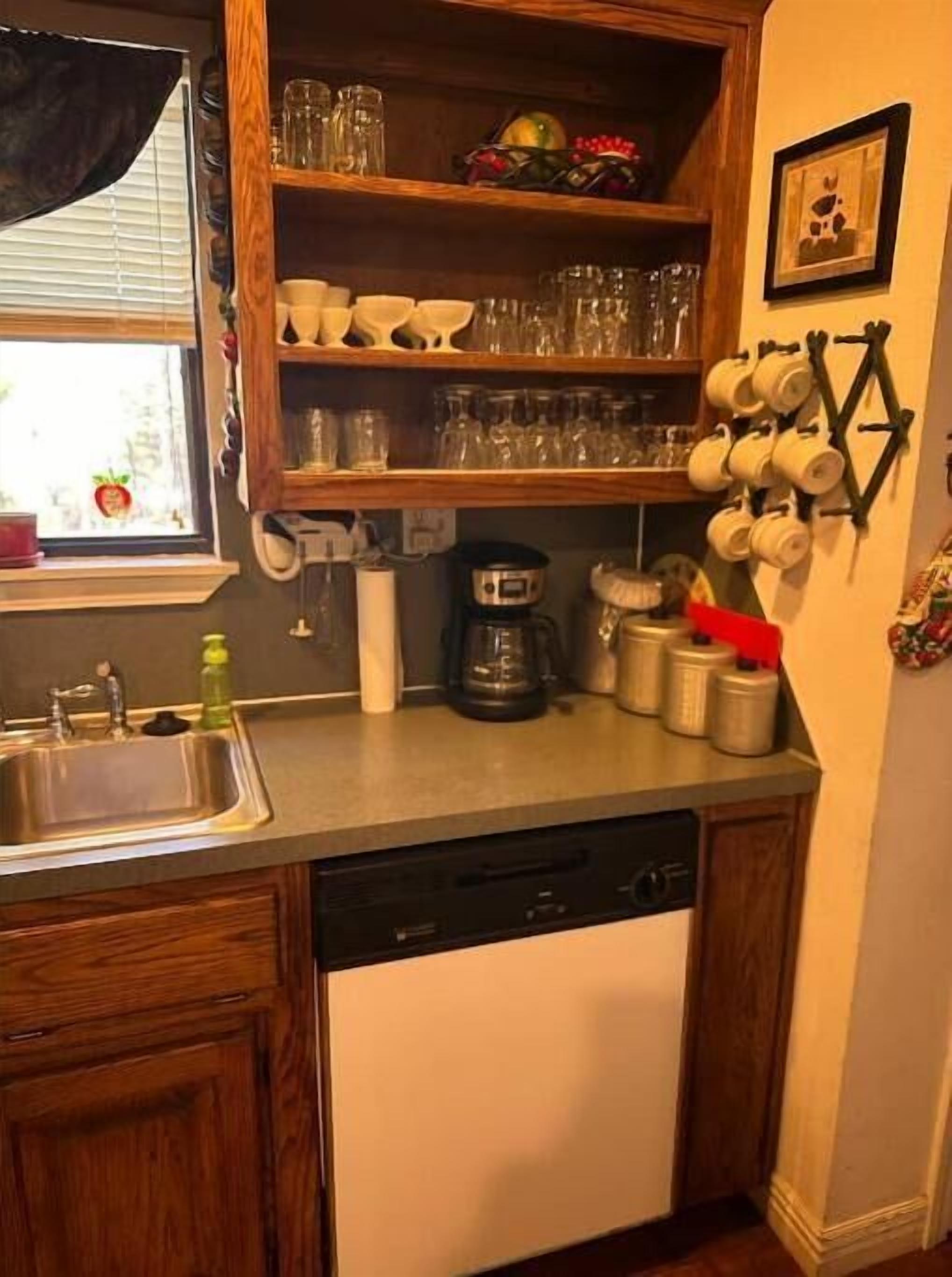 A kitchen with wooden cabinets, a dishwasher, a coffee maker, and a mug rack on the wall.