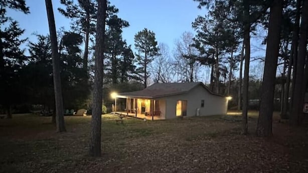 A small, single-story house with a porch and a covered outdoor seating area, surrounded by trees.