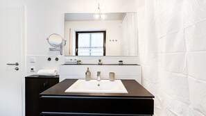 A modern bathroom with a large sink, dark vanity, and a mirror above it. There are two small potted plants on the vanity, and a window with curtains is visible in the background. - A-citynetflixboxbetten -sofainnenstadtparkmöglichkeitenvollausstattungneu! (Augsburg)
