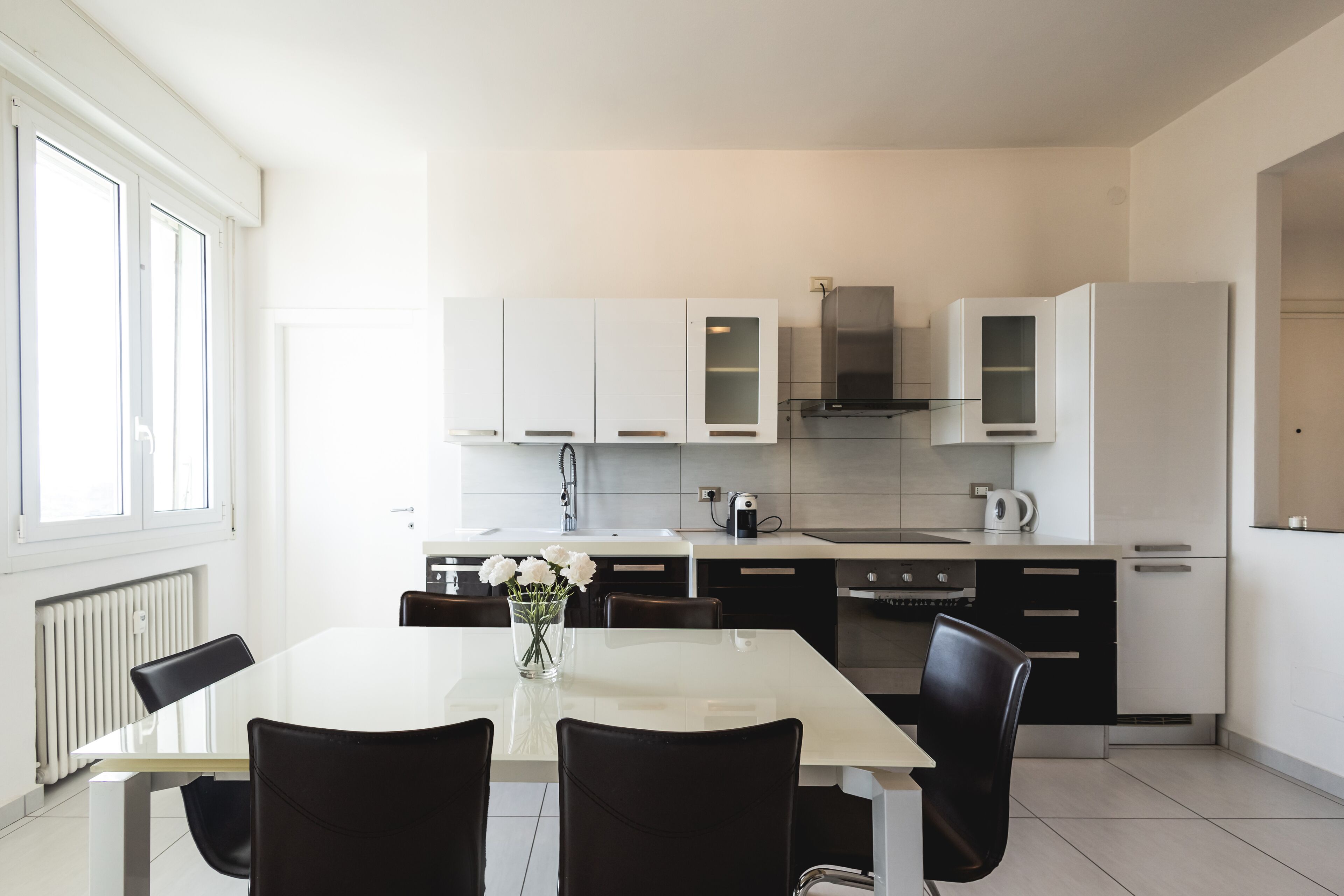 Una cocina moderna con armarios blancos, una campana extractora de acero inoxidable y una mesa de comedor blanca con sillas.