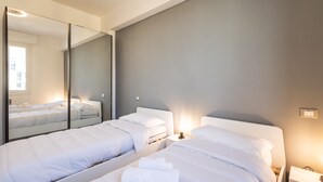 A modern hotel room with two beds, a large mirror, and a bedside table with a lamp. - Ravenna Sky View Apartment (Ravenna)