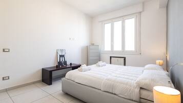 A modern bedroom with a large bed, a bedside table, a desk, and a window.