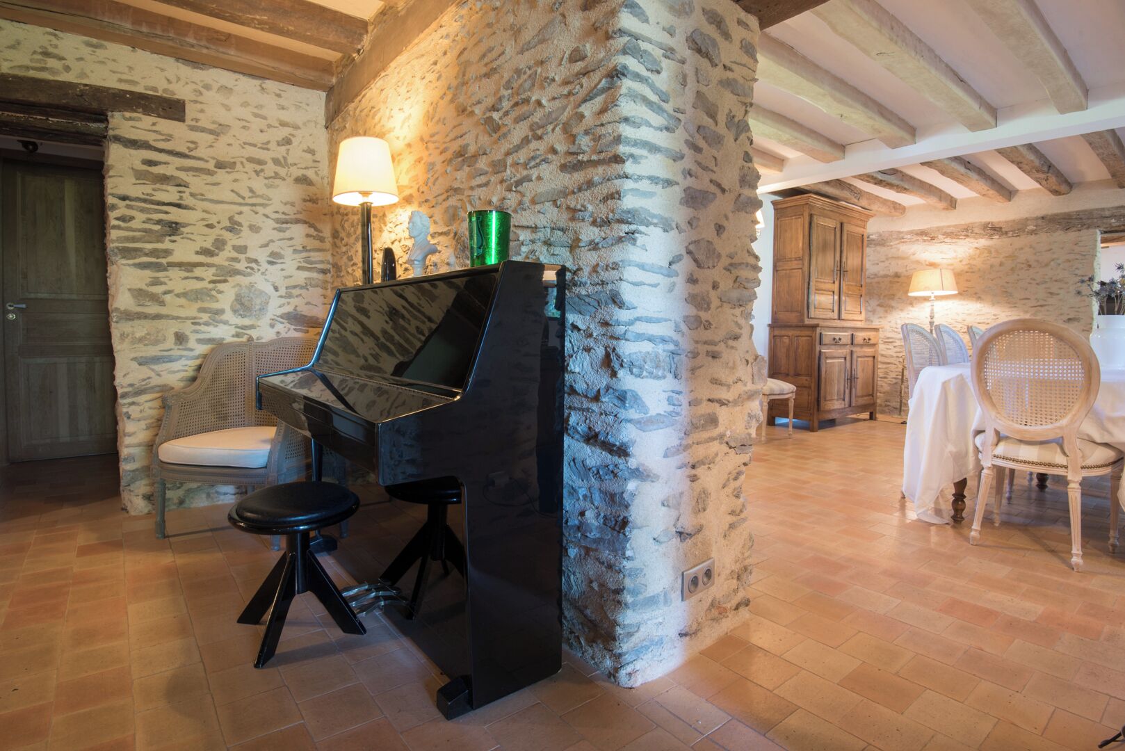 Une pièce avec un piano, des murs en pierre, des meubles en bois et un coin repas.