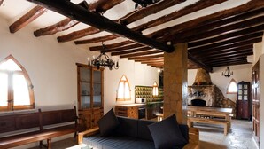 Un intérieur rustique avec des poutres apparentes, une cheminée en pierre et un coin salon confortable agrémenté d’un banc et d’un canapé.