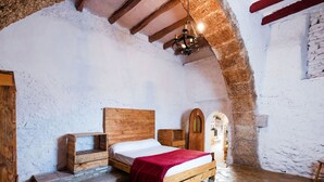 Une chambre à coucher rustique avec un sol en pierre, un cadre de lit en bois et une couverture rouge.