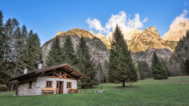 A stone cabin with a wooden porch, surrounded by a grassy field and tall pine trees, with a mountain range in the background. - Wonderful private villa for 6 guests with TV and pets allowed (Massimeno)