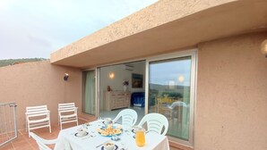 A dining area with a table set for four, chairs, and a glass sliding door leading to a room with a bed and a painting. - Cosy apartment in villa for 5 guests with A/C, pool, WIFI, TV, terrace and panoramic view (Palau)