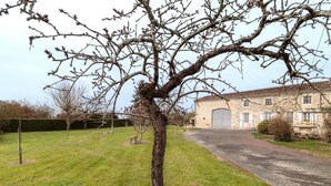 Un bâtiment en pierre doté d’un grand portail de garage, entouré d’une pelouse et d’un arbre sans feuilles.