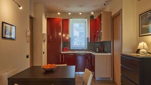 Una cucina compatta con pensili e basi rossi e in legno, un tavolo da pranzo con sedie e un piccolo finestrino.