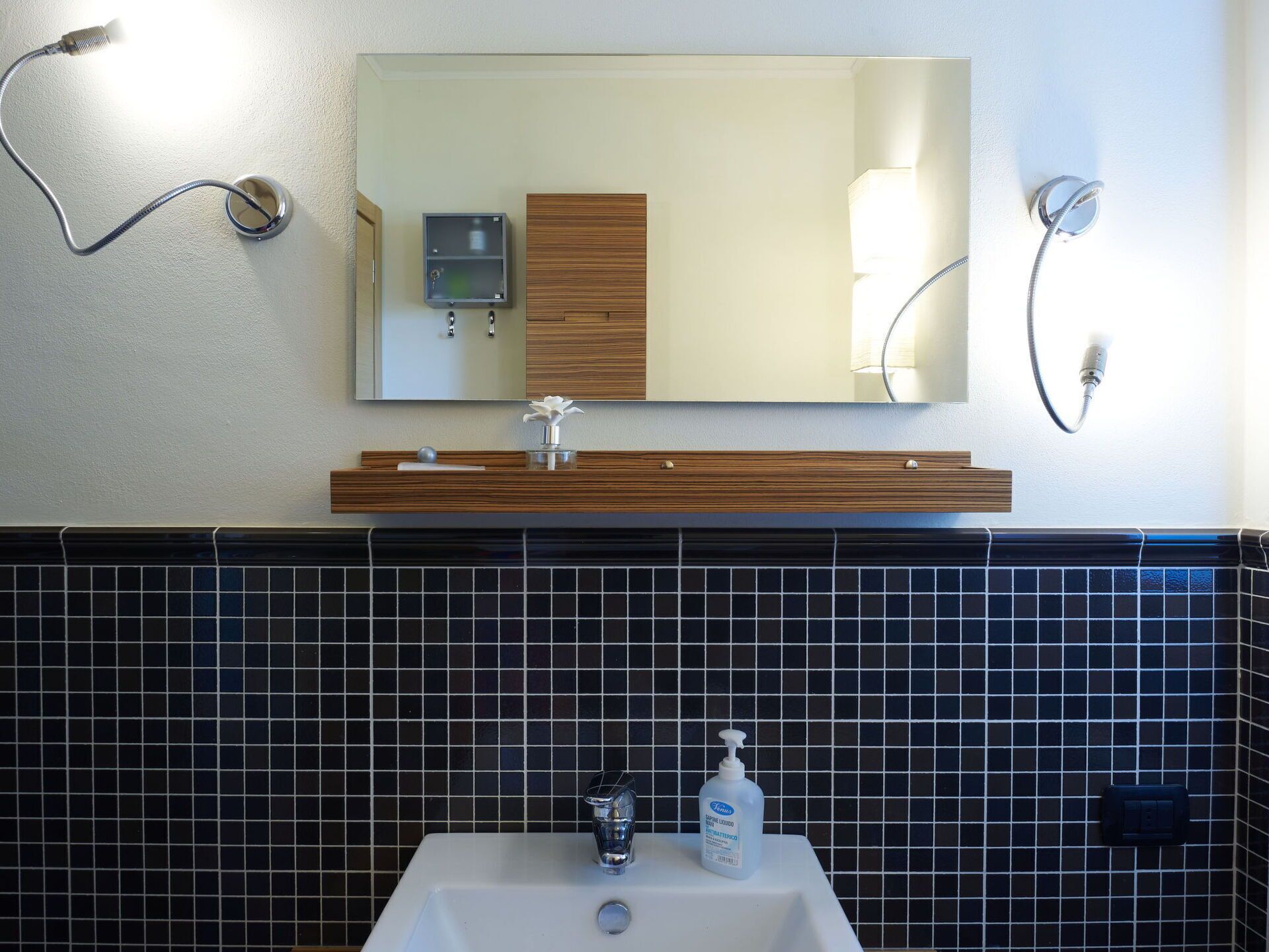 Een badkamer met een witte wastafel, een spiegel erboven en een houten wastafelmeubel.