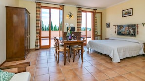 Une chambre avec un lit, une table à manger et des chaises, une armoire en bois et un balcon avec des rideaux.