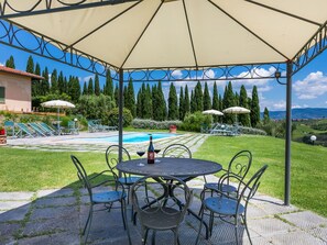 Ein überdachter Außenbereich mit Pool, Liegestühlen und einem Tisch mit Stühlen.