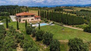 Une grande maison avec une piscine, entourée d’une végétation luxuriante et de vignobles.